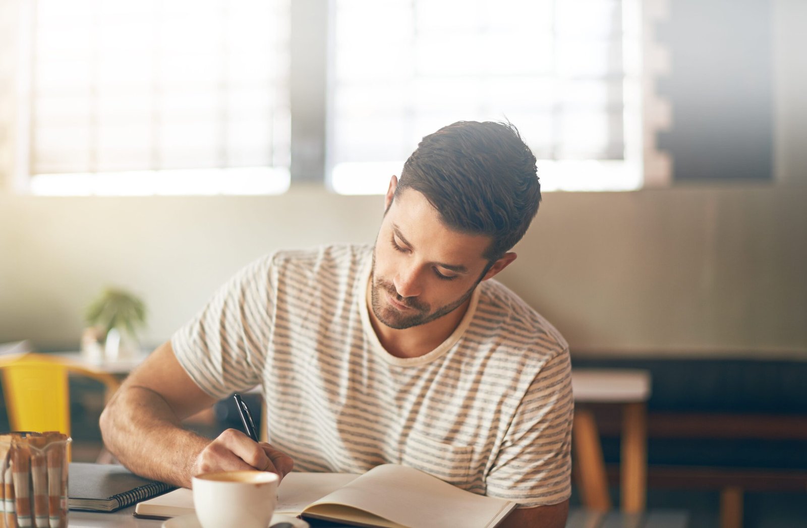 “Write My Lifestories” – Man Actively Documenting His Family History A man with a light beard sitting at a desk, looking down and actively writing in a journal or notepad with a pen.